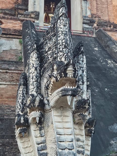 A five-headed naga in white stucco streaked black by rain, at the foot of one of the chedi's stairways