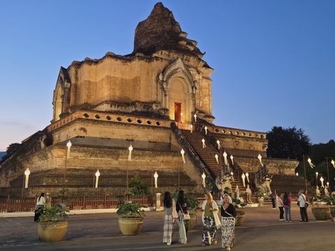 The whole chedi floodlit at dusk, with a group of visitors walking across the forecourt in front of it and others standing at the foot of its east stairway