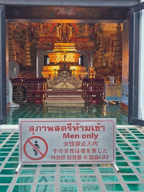 The open door of the city pillar shrine, a gilded tiered structure inside, and in front a sign in Thai, English, Chinese, Japanese and Korean reading Men only
