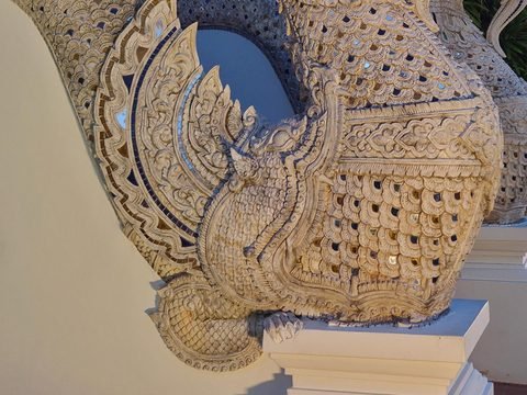 The foot of a stucco stair balustrade: a scaled creature with a large round eye, flame-shaped fins set with mirror glass and a clawed foot on the plinth, under the scaled body of the naga