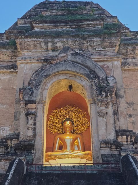 A lit niche in the chedi's weathered brick: a seated gilded Buddha in front of a gilded tree, under a worn stucco arch