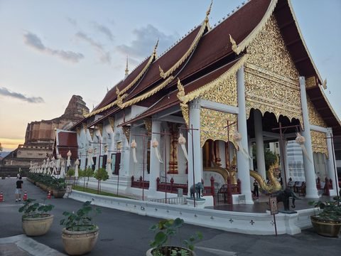 The long Wihan Luang with its stacked roofs and gilded gable, and on the left in the distance the broken top of the chedi, early evening