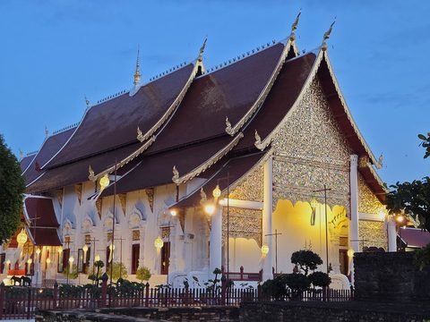The Wihan Luang lit up after dusk, its silver and gold gable glowing, lamps along its white walls
