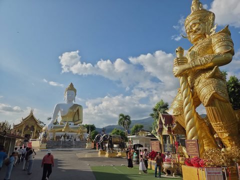 The forecourt of the summit: a giant gilded guardian statue in the foreground, the big white-and-gold Buddha in the distance, visitors and small shrines between them