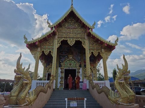 A gilded hall with a tiered roof, reached by a stair flanked by two large golden nagas; two monks in saffron robes stand in the doorway