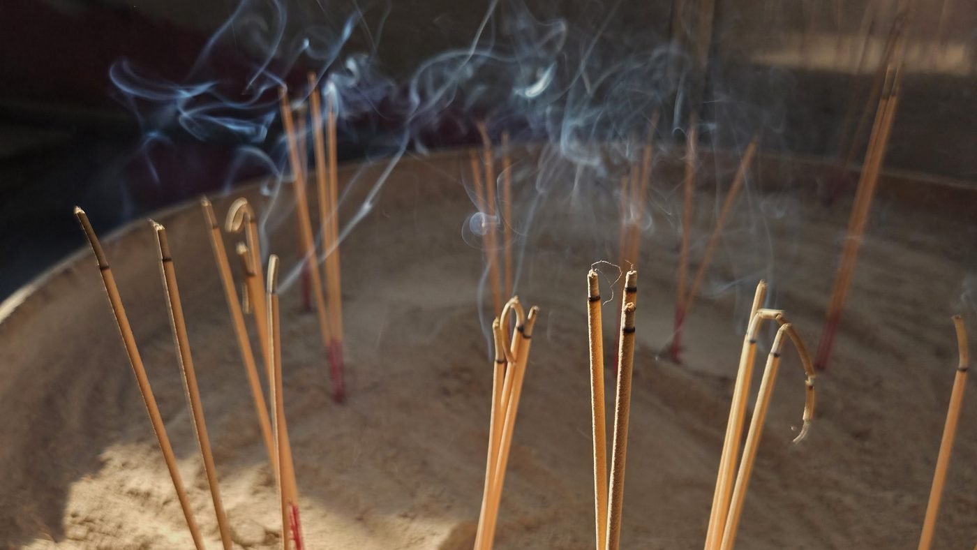 Incense sticks planted in a bowl of sand; the smoke curls up into the light