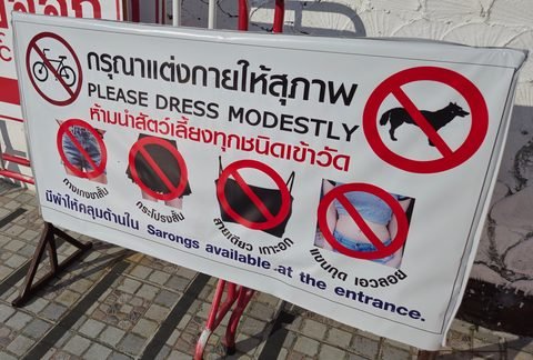 A sign headed Please dress modestly, with crossed-out pictograms for shorts, short skirts, strappy tops and pets, and the line Sarongs available at the entrance