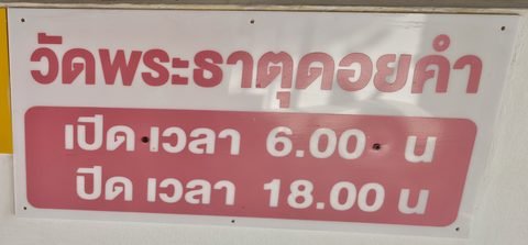 A red-and-white sign in Thai: Wat Phra That Doi Kham, opens 6.00, closes 18.00