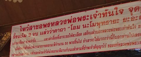 A white banner with red Thai lettering, stretched under the roof of the hall; its right edge is out of frame