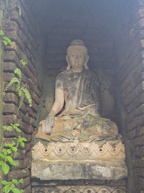 Un Bouddha assis, patiné, dans une niche de brique, la main droite posée sur le genou, doigts vers le sol, quelques paillettes de feuille d'or sur le visage