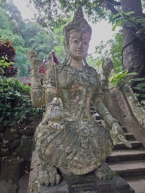 La statue moussue d'une figure couronnée au buste humain et au corps de lion, un objet dans chaque main, au bord d'un escalier de brique ; une plaque à ses pieds
