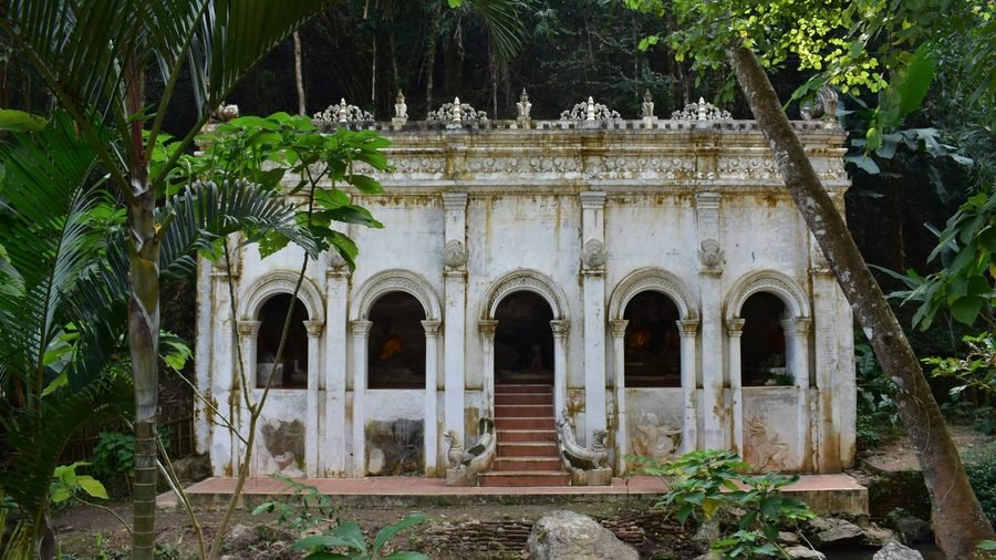 Wat Pha Lat: a weathered white temple hall with arched openings and red steps, in the forest