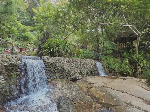 L'eau franchit un déversoir de pierre et s'étale sur une large dalle de roche grise inclinée, devant la forêt