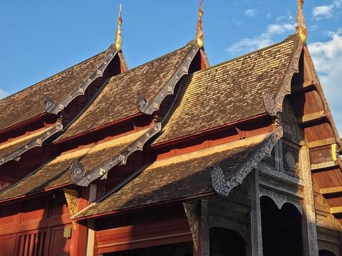 The stepped roofs of the ubosot against a blue sky: small overlapping tiles, carved bargeboards ending in curls and gilded finials