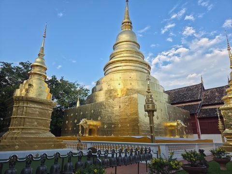 The gilded chedi with gilded elephant figures along its base, a smaller chedi on the left and a row of bells in front