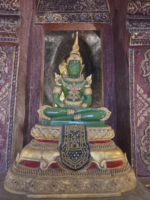 A green, crowned and jewelled seated Buddha image in a niche inside the ubosot