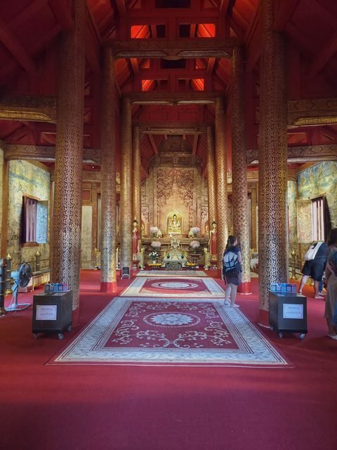 Inside the Wihan Lai Kham: red pillars covered in gold stencil lead to the altar, with painted walls on either side
